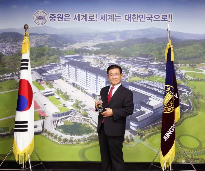 황윤원 총장이 중원대학교 캠퍼스 그림 앞에서 상패를 들고 서 있는 모습